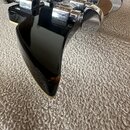 Záběr na zadní stranu černé hlavy elektrického nástroje s chromovanými ladicími kolíky. Povrch laku je glossy a vykazuje odrazy okolí. Na spodní hran…