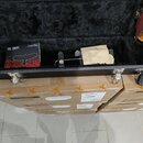 Otevřený černý nástrojový kufr s vnitřním čalouněním z černého plyšového materiálu. Uvnitř je umístěno balení strun s nápisy „PR“, „PBS“ a „Signature…