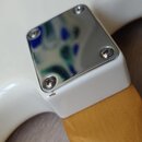 Detail krku elektrické kytary v místě spoje s bílým tělem. Je zde vidět chromovaný kryt upevněný čtyřmi šrouby, pod kterým je zakrytý spoj krku s těl…