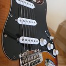 Elektrická kytara s tylem z tmavého dřeva a tělem v červenohnědém sunburst provedení. Nástroj má černý pickguard, tři bílé snímače typu single-coil a…
