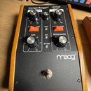 Černý efekt pedál s dřevěnými bočními stěnami. Na horním panelu jsou nápisy moogerfooger® LOWPASS FILTER a logo moog®. Zařízení má čtyři ovládací kno…