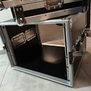 Černý transportní kufr s hliníkovými hranami a kovovým kováním. Vnitřek je vyložen černým materiálem a obsahuje dva vestavěné kovové konektory. Na hl…