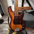 Elektrická basová kytara s trupem v červenohnědém sunburst provedení a hnědým hmatníkem. Nástroj má tmavě červený tortise pickguard a je vybavený dvě…