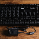 Černý hybridní bicí automat KORG drumlogue HYBRID DRUM MACHINE. Zařízení má mnoho ovládacích knoflíků, tlačítek a v pravé části displej. Před přístro…