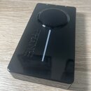 Černý obdélníkový přístroj s lesklým povrchem. Na horní straně je umístěn velký kulatý ovladač a vedle něj dvě malé kontrolky. Na přední straně je vy…