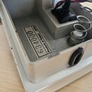 Detail vnitřku stříbrného kovového šasi efektového pedálu. Na vnitřní straně je nalepený štítek s nápisem Products of Roland JAPAN a číslem 634000. V…