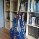 Modrá polodublová elektrická kytara s chromovaným hardwarem a bílým ráfkem kolem těla. Na krytu snímače je viditelný nápis GRETSCH a na hlavě hředu j…