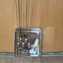 Detailní pohled na spodní část akustické kytary se světlým dřevěným povrchem. Vidět je kovová kotva strun s několika kovovými kolíky. Struny jsou v m…