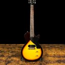 Elektrická kytara s jednobodovým snímačem v pozici hradle a černým pickguardem. Tělo má barevný přechod od žluté k tmavě hnědé (sunburst). Na hlavě j…
