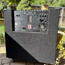 Zadní strana basového komba s černým textilním potahem a plastovými rohovými chráničmi. Na zadním panelu je nápis 120 Watt FET Bass Guitar Amplifier…