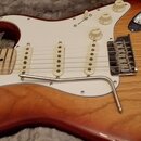 Elektrická kytara s trupem v červeně-žlutém sunburst provedení a bílým pickguardem. Nástroj má tři bílé snímače typu single-coil, jeden tónový potenc…