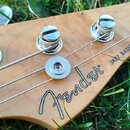Záběr na hlavu basové kytary z přírodního dřeva s viditnou masivní strukturou. Na zadní straně je černý nápis Fender® JAZZ BASS®. Jsou vidět čtyři ko…