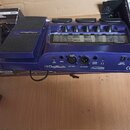 Modrý kytarový procesor značky Digitech s nápisem Audio DNA. Na zadní straně jsou viditelné vstupy a výstupy s popisky CD INPUT, INPUT, MIC INPUT, MI…