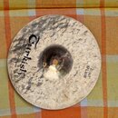 Kovový činel typu splash s výrazně kladeným povrchem v přirozené zlatavé barvě. Na povrchu je černý nápis „Turkish“ a menší text „Handmade quality fr…