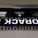 Fotografie zachycuje zadní stranu rackového mixážního pultu černé barvy s kovovými úchyty po stranách. Na spodní části je nápis EURORACK PRO PROFESSI…