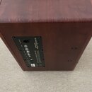 Zadní strana hnědého kytarového komba s dřevěným povrchem. Na černém zadním panelu jsou nápisy JOYO BSK-80 a 80 WATT ACOUSTIC GUITAR AMPLIFIER. Jsou…