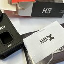 Černý kožený držák na vysílač s logem Xvive a označením H3. Vedle něj je položen bílý papír s logem Xvive a webovou adresou www.xvive.com, černý manu…