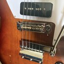 Detail korpusu elektrické kytary v hnědé barvě s bílým pickguardem. Jsou vidět dva černých humbuckery, chromovaný kobylník a chromovaný stupňovitý mo…