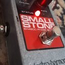 Šedý efekt pedál s nápisem electro-harmonix na spodní části. Na horním panelu je červené pole s bílým textem SMALL STONE a EH4800 PHASE SHIFTER. Zaří…