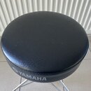 Černý polstrovaný hudební taburet s kulatou sedací plochou z koženky. Na boku je vidět šedý nápis YAMAHA s doprovodným logem. Podsedák je upevněn na…