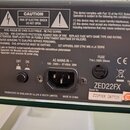 Záběr na zadní panel černého elektronického zařízení. Je zde vidět napájecí konektor, vypínač a pojistka s nápisem FUSE T1A L 250V 20mm. Na panelu je…