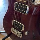 Tmavě červená elektrická kytara s hnědým hmatníkem a bílými tečkovanými značkami. Nástroj má dva humbuckery s chromovaným rámečkem, fixní most a dva…