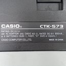 Fotografie detailu černého plastového štiketu s technickými údaji. Je na něm uveden název značky CASIO® a model CTK-573. Text dále obsahuje nápisy RA…