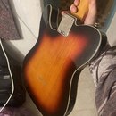 Zadní strana elektrické kytary s tónem sunburst (přechod od černé k žluté) a bílým lemováním. Na kovové krytce krkovnice je vyryto logo "Telecaster".…