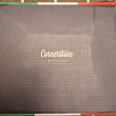 Černá papírová krabice s bílým nápisem Cornerstone MUSIC GEAR uprostřed. Horní a dolní hrana krabice je opatřena barevným pruhem v barvách zelené, bí…
