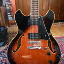 Polodupatá elektrická kytara s tělem v provedení sunburst (oranžová a černá). Nástroj má dva humbuckery, černý plechový pickguard a čtyři ovládací kn…