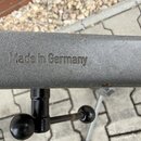 Detailní záběr na šedý kovový profil s texturou. Na povrchu je vyražen nápis Made in Germany. K profilu jsou připevněny černé plastové knoflíky a šro…