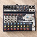 Černý mixážní pult s bílými a šedými popisky. Na předním panelu je vidět značka Soundcraft a název modelu NOTEPAD-12FX, dále nápis Lexicon EFFECTS a…