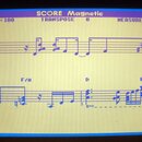 Fotografie zachycuje displej s digitálním zobrazením notového zápisu. V horní části je nápis SCORE Magnetic, TEMPO J = 100, TRANSPOSE 0 a MEASURE 009…