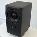 Černý studiový subwoofer v hranatém korpusu s odsazeným předním panelem. Na spodní části přední strany je umístěn štítek s nápisy "S/N: [nečitelné]"…