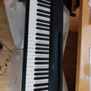 Černý digitální klavír s bílými a černými klávesami. Na horním panelu je uprostřed bílé barvy nápis YAMAHA s doprovodným logem. V levé části panelu j…