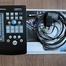Černý kontrolér PreSonus FADERPORT Production Controller s řadou tlačítek a posuvníkem na levé straně. Vedle zařízení je položen jeho původní kartono…