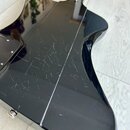 Zadní strana elektrické kytary s černým lesklým povrchem. Lak je v oblasti těla výrazně poškrábaný a obsahuje numerous drobné rýhy. Na fotce nejsou ž…