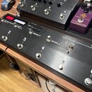 Černý efektový spínací systém s nápisem BOSS ES-8 EFFECTS SWITCHING SYSTEM. Zařízení má osm kovových spínacích tlačítek, z nichž šest je očísleno čís…
