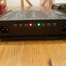 Černý kovový box s ovládacími prvky a konektory. Na horní straně je schéma a nápisy: OUTPUT 2, PHASE, FILTER, GROUND, BATTERY, POWER, GROUND, FILTER,…