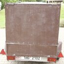 Hnědý transportní kufr z dřevěného nebo kompozitního materiálu s kovovými hranami a zapojovacími prvky. Povrch je viditelně opotřebovaný, s mnoha škr…
