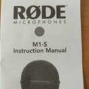 Fotografie znázorňuje bílý papírový návod k použití. Je na něm černý nápis RØDE MICROPHONES, označení modelu M1-S a text Instruction Manual. Ve spodn…
