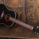 Černá akustická kytara s hnědým rýhovaným plechtrem a bílým lemováním korpusu. Na hlavě nástroje je zlatý nápis Gibson. Hриф má tmavou hmatovnici s j…