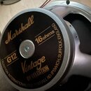 Fotografie zachicuje zadní stranu reproduktoru s kovovým rámem. Na černé krytce magnetu jsou zlatým písmem nápisy Marshall, G12, 16 ohms a Vintage BY…