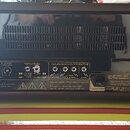 Zadní strana kytarového zesilovače Hughes & Kettner s černým povrchem. Na zadním panelu jsou nápisy REVERB BALANCE, FX-LOOP, FOOTSWITCHES a LOUDSPEAK…