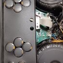 Fotografie zachycuje vnitřek elektronického zařízení s černým kovovým šasi a dvěma velkými kulatými reproduktory. Na šasi je umístěno deset černých v…