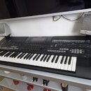 Černý digitální klavír s bílými a černými klávesami, umístěný na bílém stole. Na horním panelu jsou nápisy YAMAHA, 10th ANNIVERSARY a modelové označe…