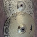 Dvě kovové činely položené na hnědém laminátovém povrchu. Spodní činel má černý nápis PAiste 302 a pod ním menší text 14" HI-HAT Bottom. Horní činel…