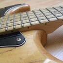Detail elektrické kytary s přírodním dřevěným povrchem těla a hnedem hрифem. Na kytaru je nasazen černý pickguard. Povrch laku na těle vykazuje vidit…