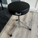 Černý bubeníckýstolek s kulatým polstrovaným sedadlem a chromovanou třínohou základnou. Na boku sedadla je bílý nápis Pearl. Povrch sedadla i chromov…