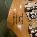 Záběr na zadní stranu dřevěné hlavy nástroje s třemi kovovými ladicími mechanismy. Na povrchu je černý nápis „Designed and Backed by Fender“, „Crafte…